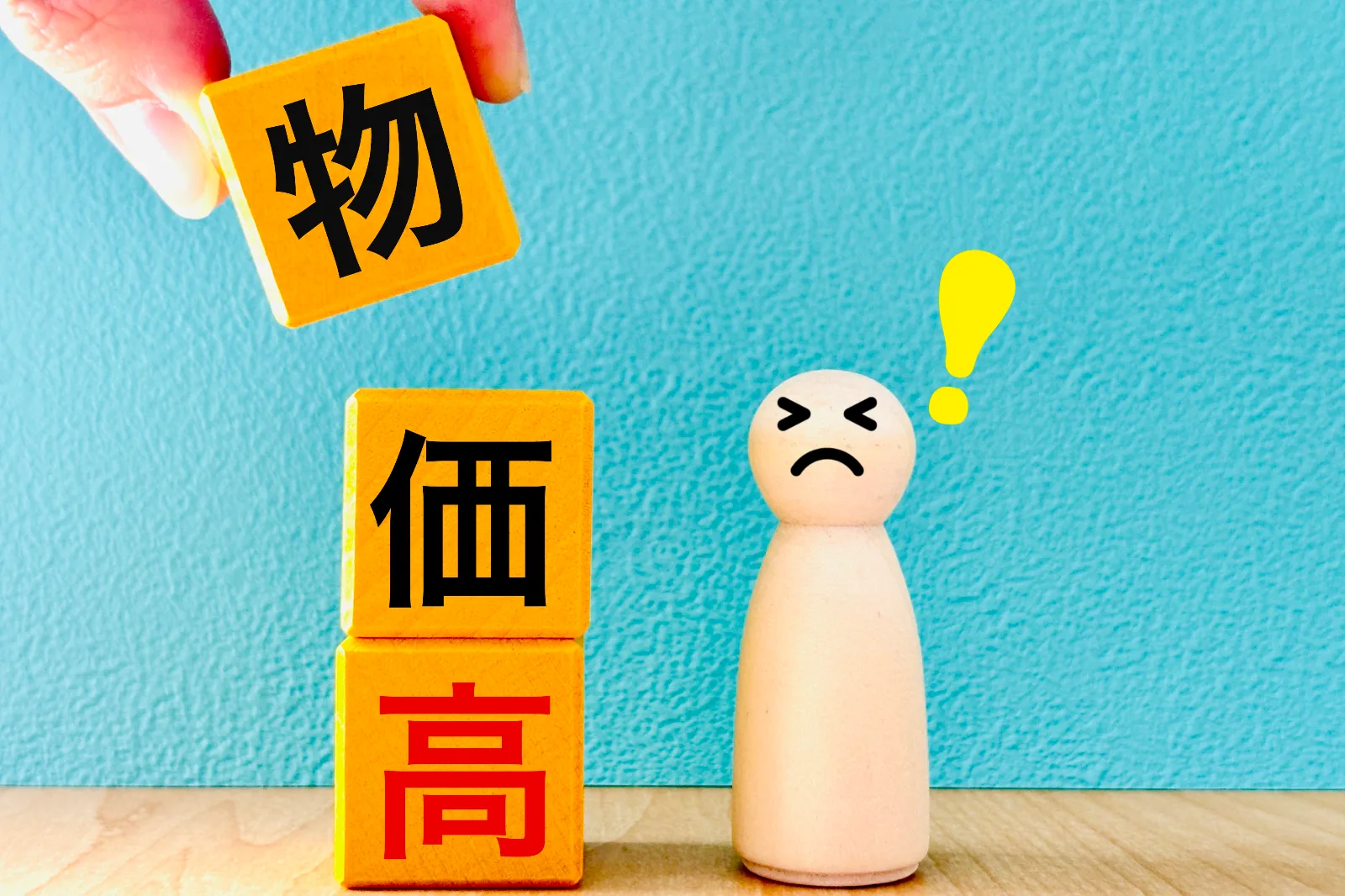 「値上げ」と並べた木のブロックと、その横で頭を抱える人形